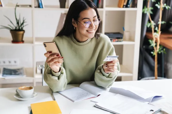 A student at her desk pays for course materials with a bank card and phone.
