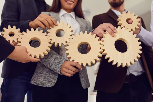 Colleagues fit large wooden gears together, meshing like connected systems.